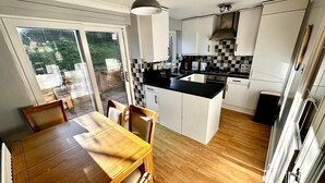 A kitchen with a dining area, featuring a large island, white cabinets, and a view through the sliding glass door. - Detached 3-bedroom house with garage and garden. (Droitwich Spa)