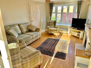 A living room with a sofa, armchairs, a television, and a patterned rug.