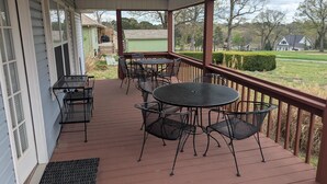 Eine überdachte Veranda mit Tisch und Stühlen, ein kleiner Grill und Blick auf ein grünes Haus und Bäume.
