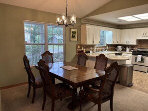 A dining area with a wooden table and chairs, a chandelier, and a kitchen with white cabinets and appliances. - 3- bedroom on the 18th fairway (Holiday Island)