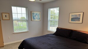 Ein Schlafzimmer mit einem großen Bett, zwei Fenstern mit Jalousien und drei gerahmten Bildern an den Wänden.