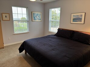 Ein Schlafzimmer mit einem großen Bett, zwei Fenstern mit Jalousien und drei gerahmten Bildern an den Wänden.