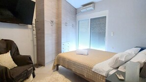 Een slaapkamer met een bed, een aan de muur bevestigde televisie, een kledingkast en een raam met zonwering.