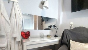 Een kamer met een wit bureau, een spiegel, een lamp, een bank en een decoratie in de vorm van een hart.