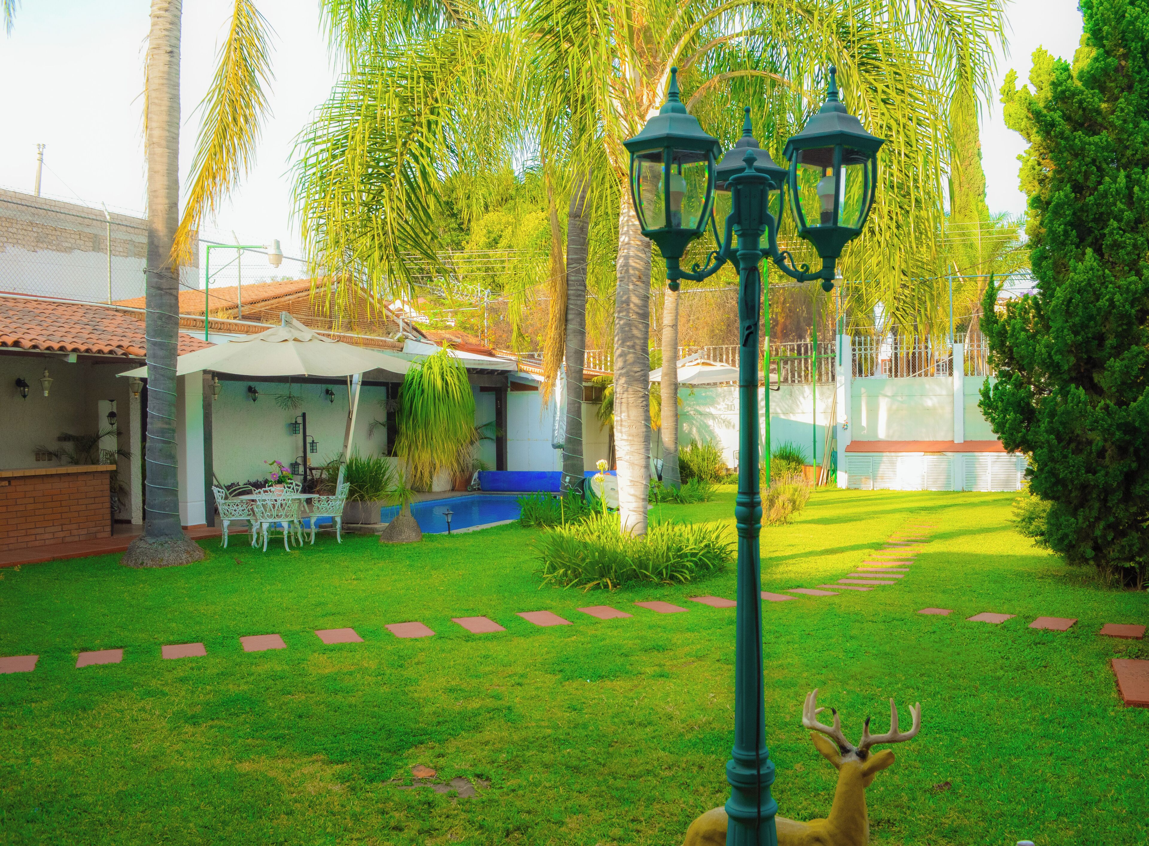 A well-maintained garden with a lawn, a deer, and a patio area with outdoor furniture.