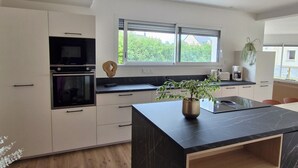 A modern kitchen with a central island, built-in oven, and a window with a view of greenery. - Ty cocon, quiet family home - near Gulf of Morbihan (Colpo)