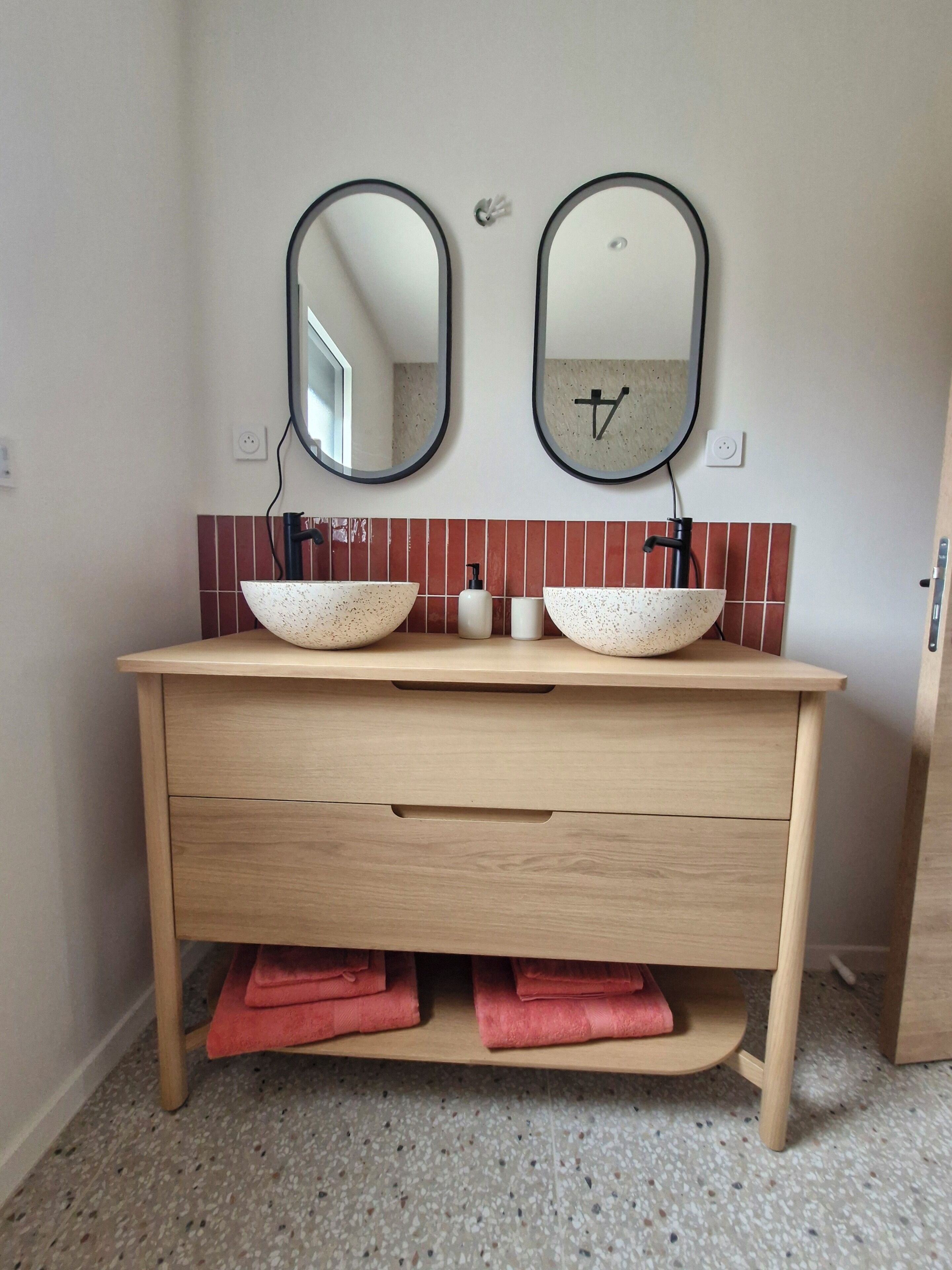 A bathroom with two vessel sinks, a wooden vanity, and a tiled backsplash.