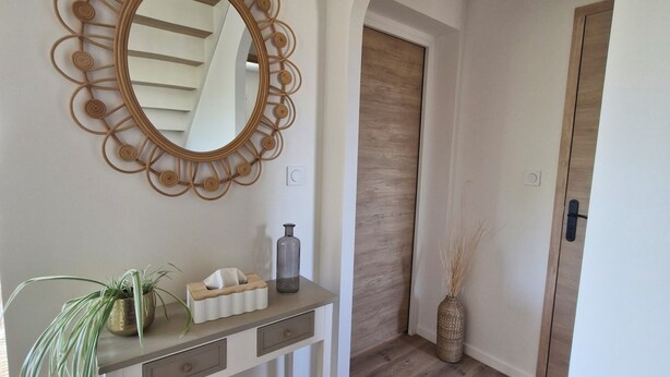 A hallway with a wooden floor, a white console table with a mirror, a plant, and a vase. - Ty cocon, quiet family home - near Gulf of Morbihan (Colpo)