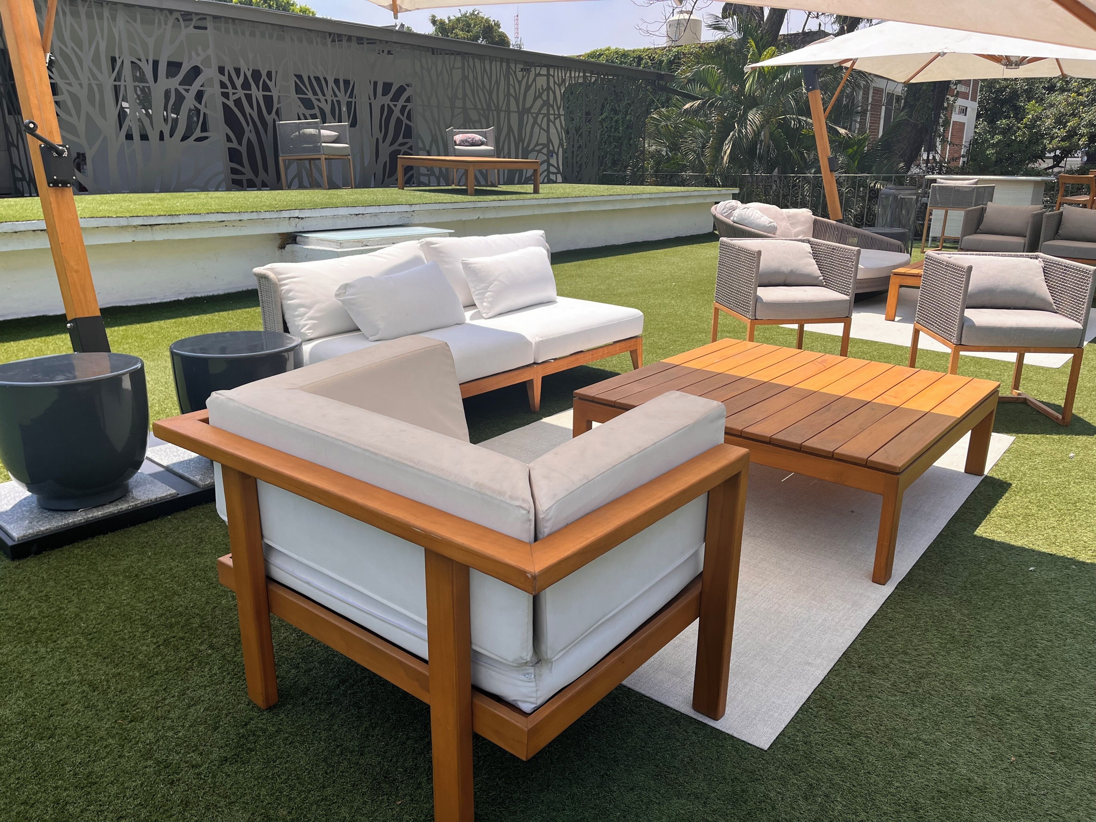 Un patio con un sofá, dos mesas de madera y sillas de mimbre.