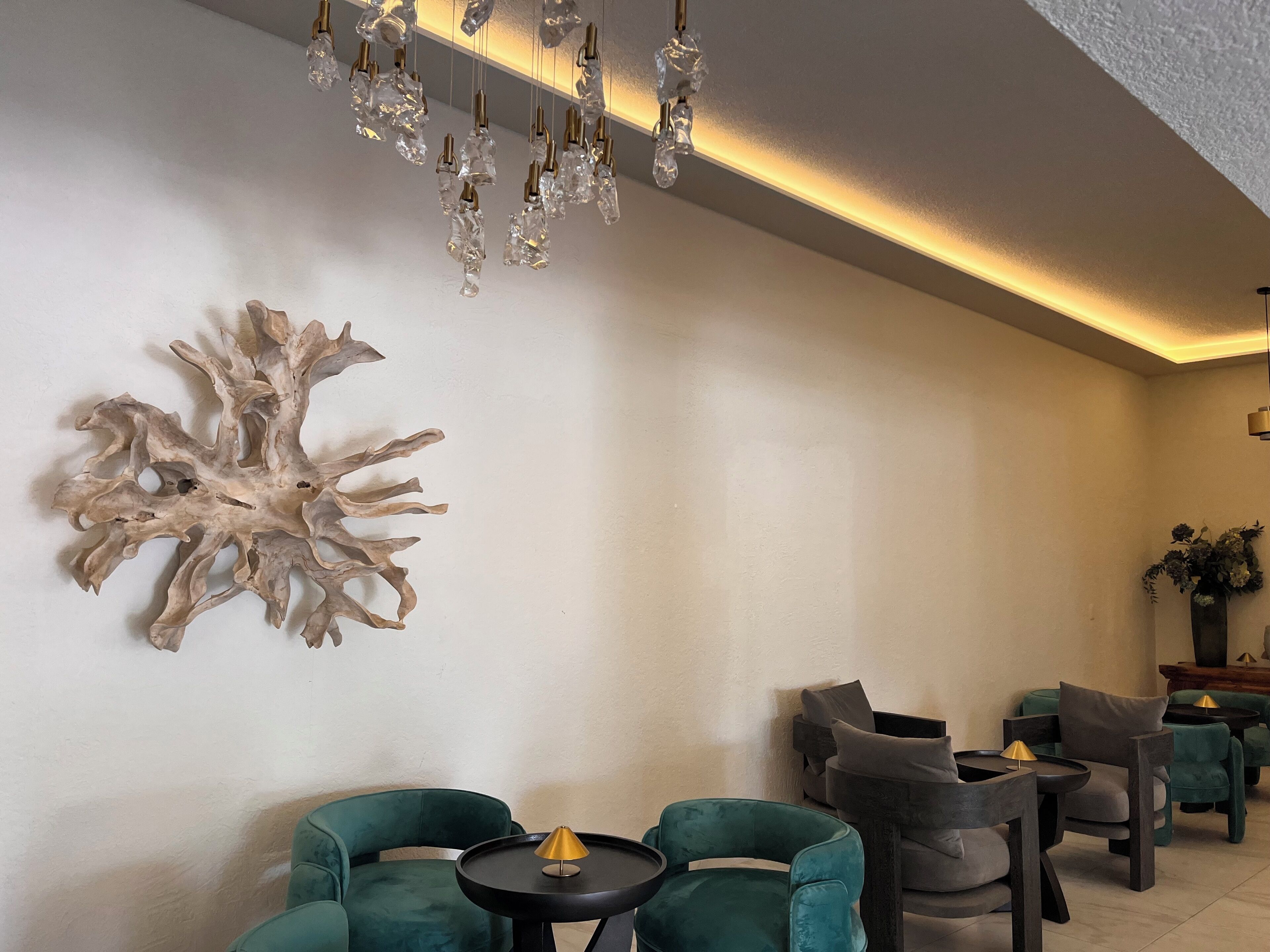 A modern interior with a unique wall art piece, a seating area with green upholstered chairs, and a ceiling light fixture.