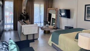 Una habitación de hotel con cama, sofá, televisión, espejo y ventana con cortinas.