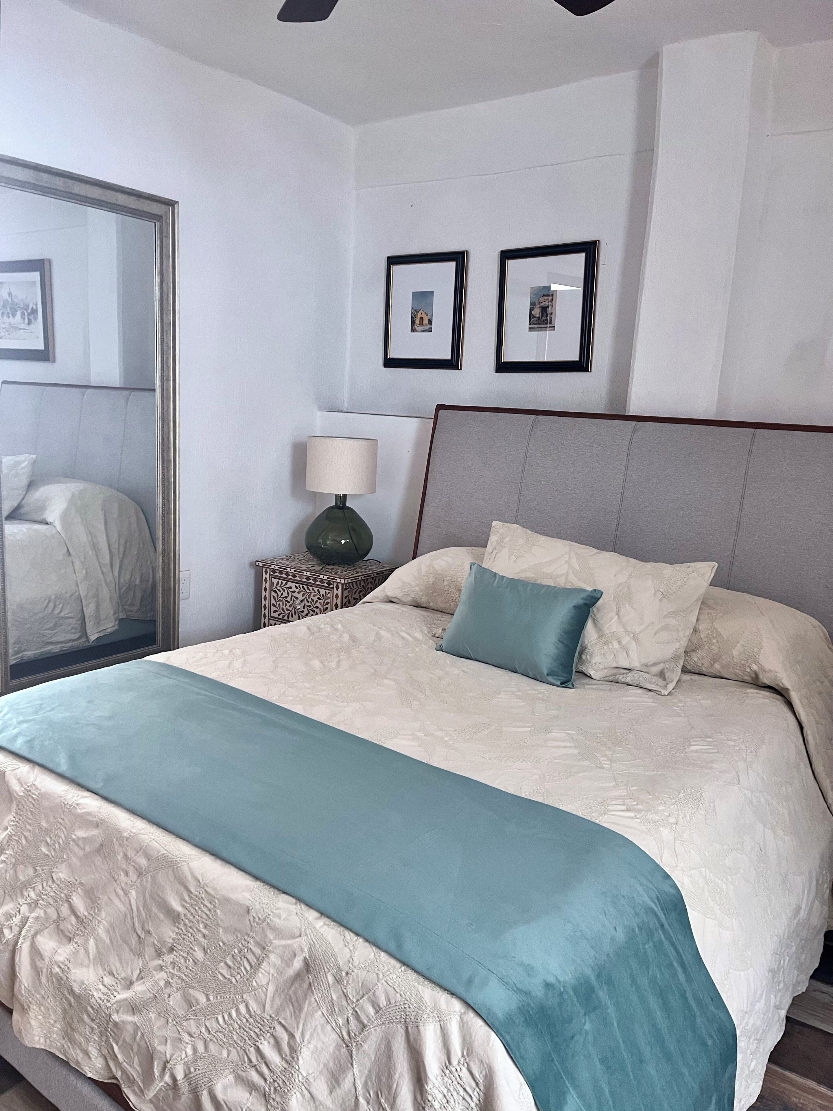 A neatly made bed with a patterned bedspread, a bedside table with a lamp, and two framed pictures on the wall.