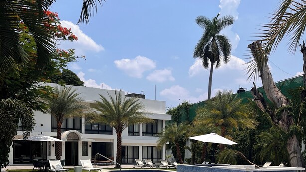 Una piscina con sillas de descanso, un edificio blanco de diseño moderno y palmeras.