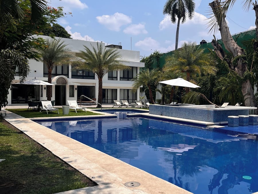 A swimming pool with lounge chairs, a white building with a modern design, and palm trees.