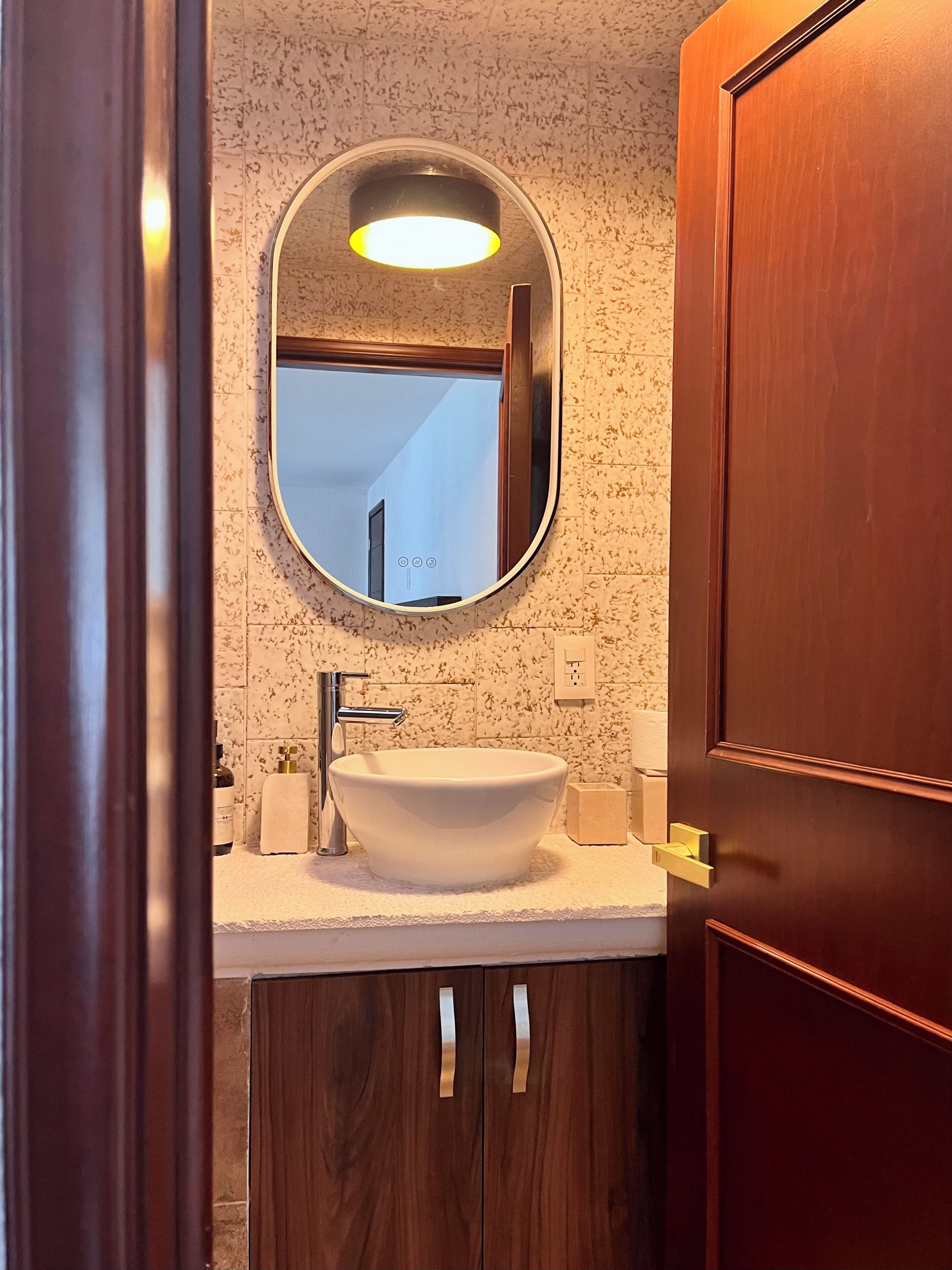 A bathroom with a round mirror, white sink, and wooden cabinets.
