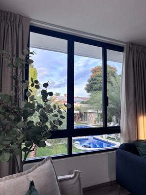 Una habitación con un ventanal grande, una planta, un sofá azul y vistas a una piscina.