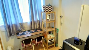 A small room with a wooden table, two chairs, a TV, a shelf with items, and a window with curtains. - Small Cosy Studio near City, Aldgate East (London)