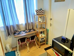A small room with a wooden table, two chairs, a TV, a shelf with items, and a window with curtains. - Small Cosy Studio near City, Aldgate East (London)