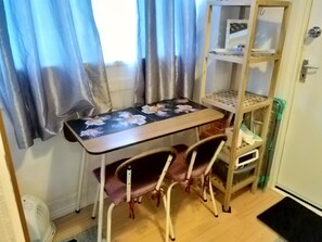A room with a wooden desk, two chairs, a small shelf with a computer, and a white door. - Small Cosy Studio near City, Aldgate East (London)