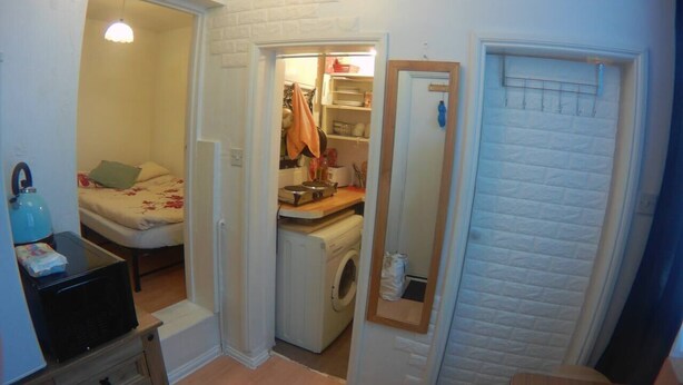 A compact room with a bed, a washing machine, a small kitchenette, and a mirror. - Small Cosy Studio near City, Aldgate East (London)