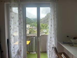 Een balkon met uitzicht op een woonwijk, een gele stoel en een tafel met spullen erop.