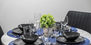 Mesa de jantar posta com tigelas pretas, copos e um pequeno vaso com planta verde no centro.