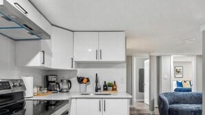 A modern kitchen with white cabinetry, a built-in oven, and a coffee maker. - The Albany Hideout - Sleeps4  - QueenBed  - NFLX&Wifi (Edmonton)