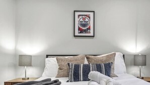 A neatly made bed with pillows, a framed picture on the wall, and two bedside lamps. - The Albany Hideout - Sleeps4  - QueenBed  - NFLX&Wifi (Edmonton)