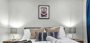 Uma cama bem arrumada com almofadas, um quadro na parede e duas luminárias de cabeceira.