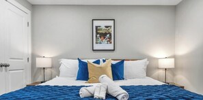 Ein Hotelzimmer mit einem Bett, zwei Nachttischlampen, einem gerahmten Bild an der Wand und einer Tür.