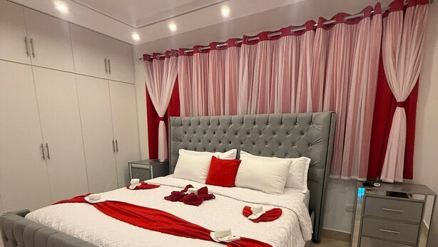 A bedroom with a large bed, a wardrobe, a nightstand, and a mirror. - VILLA GREEN PARADISE GATED COMMUNITY SECURITY 24 HOURS  (puerto plata)