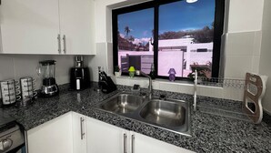 A kitchen with a granite countertop, stainless steel sink, and a window with a view of a building and trees. - VILLA GREEN PARADISE GATED COMMUNITY SECURITY 24 HOURS  (puerto plata)