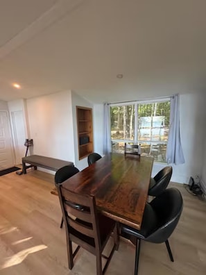 A spacious room with a large wooden table, black chairs, a bench, and a view of a forest through large windows. - Lake Rosseau Escape, 3 Bedroom, New Reno, Hot Tub! (Minett)