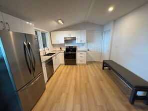 A compact kitchen with a refrigerator, stove, sink, and wooden flooring. - Lake Rosseau Escape, 3 Bedroom, New Reno, Hot Tub! (Minett)