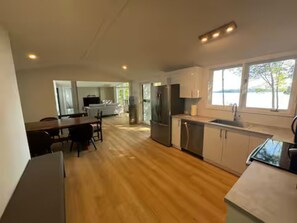A modern kitchen with wooden flooring, stainless steel appliances, and a view of the outdoors. - Lake Rosseau Escape, 3 Bedroom, New Reno, Hot Tub! (Minett)