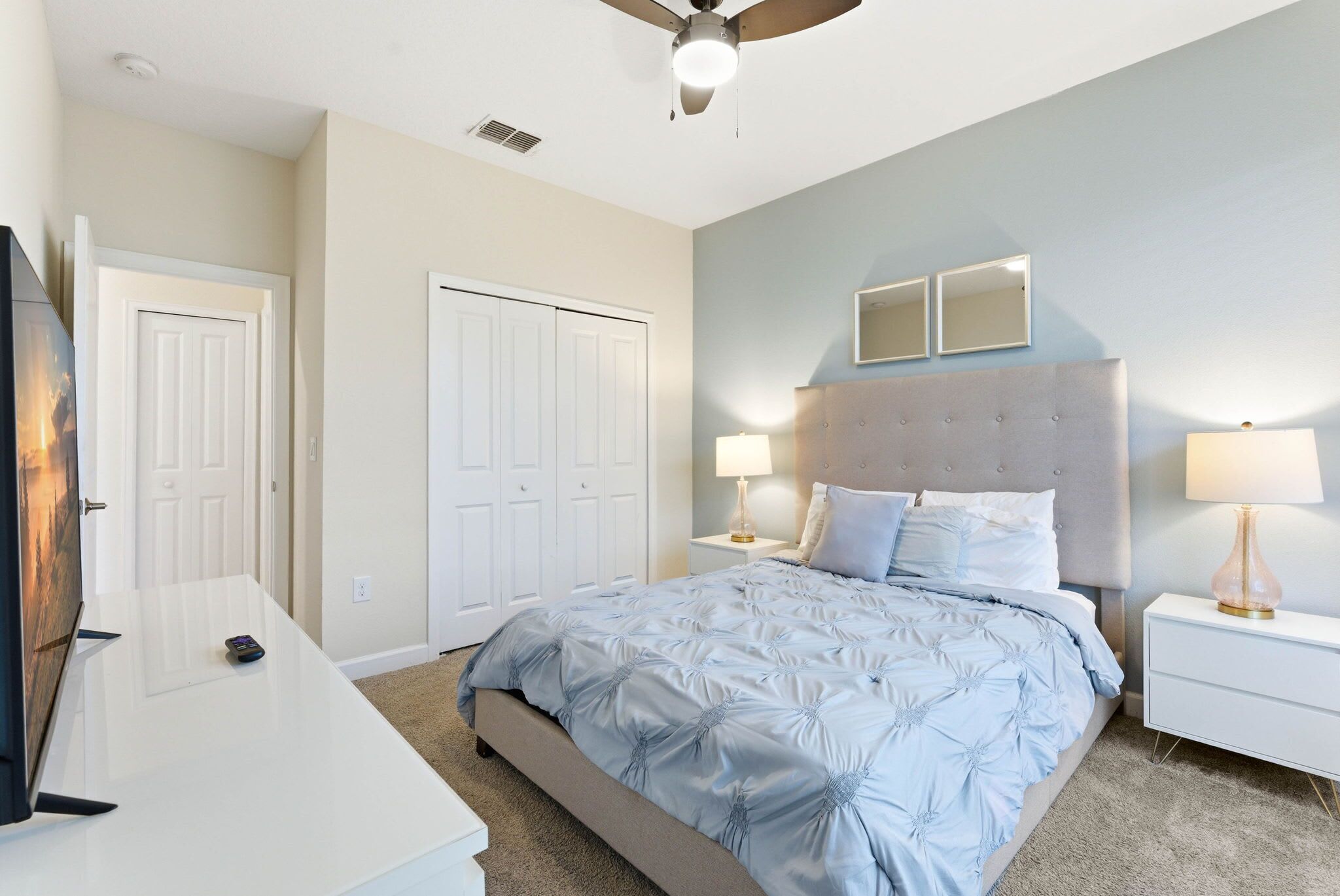 Une chambre à coucher avec un lit, deux tables de chevet avec des lampes, un ventilateur de plafond et deux portes.
