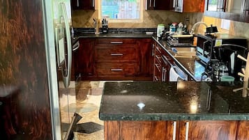 A kitchen with dark wood cabinets, a granite countertop, and a window with a view of greenery.