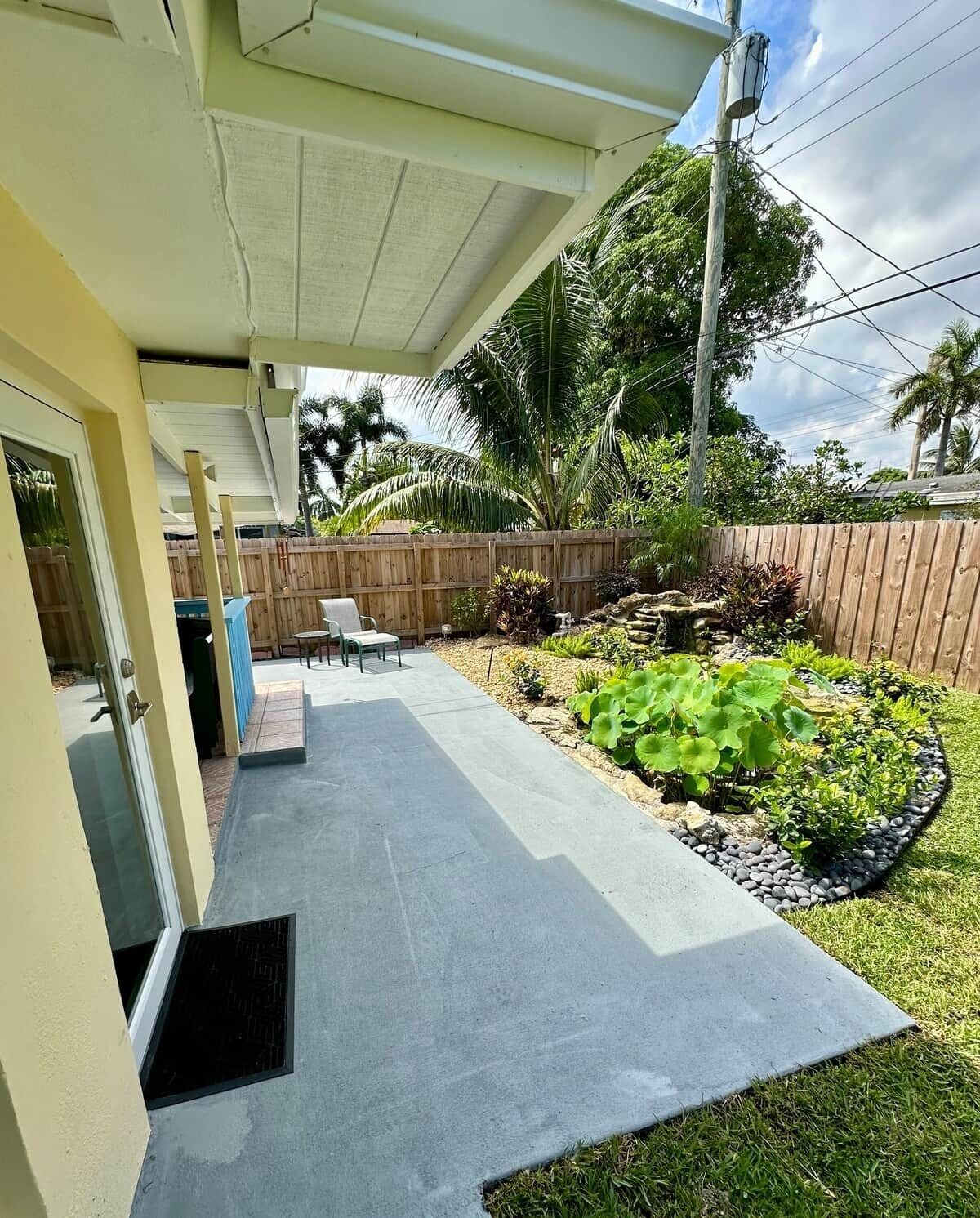 A covered patio area with a concrete floor, a wooden fence, and a garden with various plants.