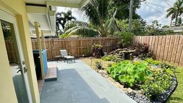 A covered patio area with a concrete floor, a wooden fence, and a garden with various plants.