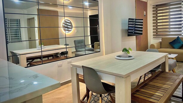 Uma sala de estar moderna com área de jantar, TV fixada na parede e um espelho grande que reflete o ambiente.