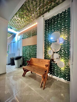 Un banc en bois dans un couloir, avec un mur recouvert de plantes vertes et un tableau blanc.