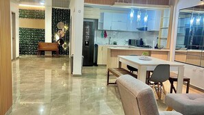Um interior moderno com piso de mármore, uma área de jantar com cadeiras estofadas em cinza, uma cozinha com armários brancos e uma parede decorativa com espelhos circulares.