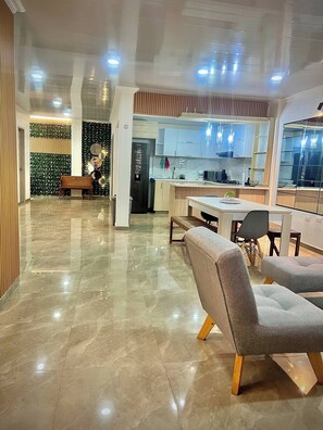 Un intérieur moderne avec un sol en marbre, un coin repas doté de chaises grises à revêtement, une cuisine avec des meubles blancs et un mur décoratif orné de miroirs ronds.