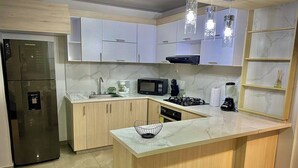 Uma cozinha moderna com armários brancos, geladeira de aço inoxidável, micro-ondas, fogão a gás e bancada de mármore.