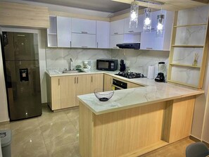 Une cuisine moderne avec des meubles blancs, un réfrigérateur en acier inoxydable, un four à micro-ondes, une cuisinière à gaz et un plan de travail en marbre.