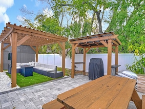 A wooden pergola with a built-in grill and seating area. - Gulf Breeze Retreat - Private 2BR/2BA  w/Fire Pit, Grill & Cozy Backyard. (New Port Richey)