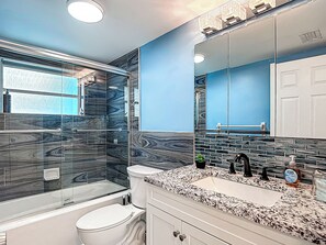 A modern bathroom with a glass shower enclosure, a white toilet, a granite countertop sink, and a large mirror. - Gulf Breeze Retreat - Private 2BR/2BA  w/Fire Pit, Grill & Cozy Backyard. (New Port Richey)