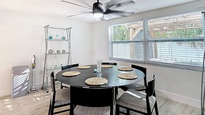 Ein Essbereich mit einem runden Tisch, Stühlen, einem Deckenventilator und einem Fenster mit Jalousien.