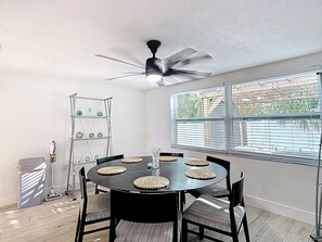 A dining area with a round table, chairs, a ceiling fan, and a window with blinds. - Gulf Breeze Retreat - Private 2BR/2BA  w/Fire Pit, Grill & Cozy Backyard. (New Port Richey)