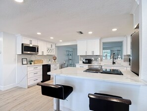 A modern kitchen with white cabinetry, a central island, a microwave, and a dishwasher. - Gulf Breeze Retreat - Private 2BR/2BA  w/Fire Pit, Grill & Cozy Backyard. (New Port Richey)